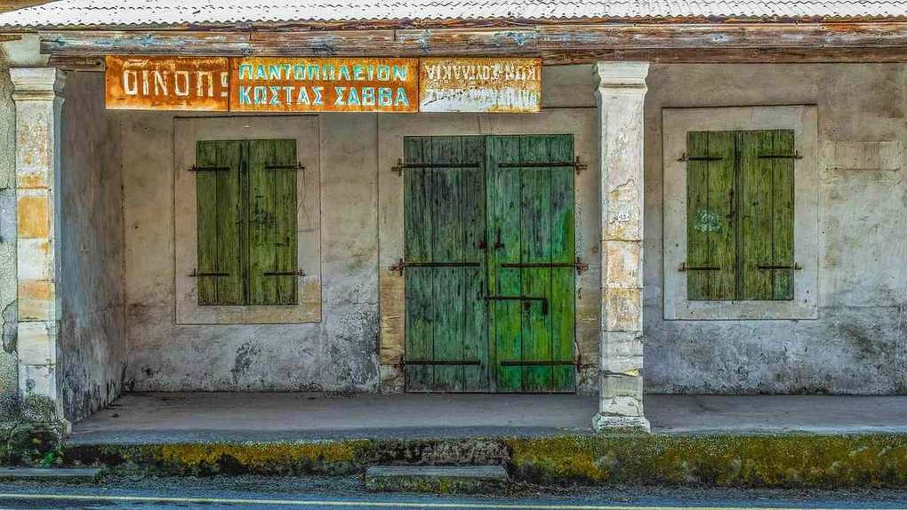 Façade usée avec enseigne en grec et trois portes vertes peintes Façade usée avec enseigne en grec et trois portes vertes peintes