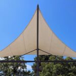 Voile triangulaire beige sur mât, arbres en dessous, ciel bleu