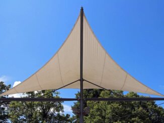 Voile triangulaire beige sur mât, arbres en dessous, ciel bleu