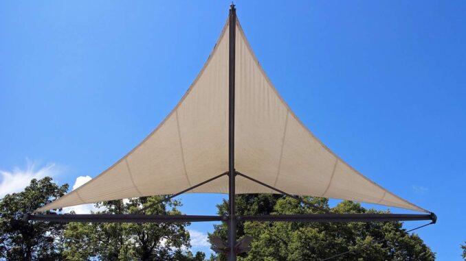 Voile triangulaire beige sur mât, arbres en dessous, ciel bleu