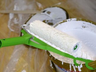 Rouleau de peinture blanc chargé de peinture blanche au-dessus d'un pot ouvert sur parquet