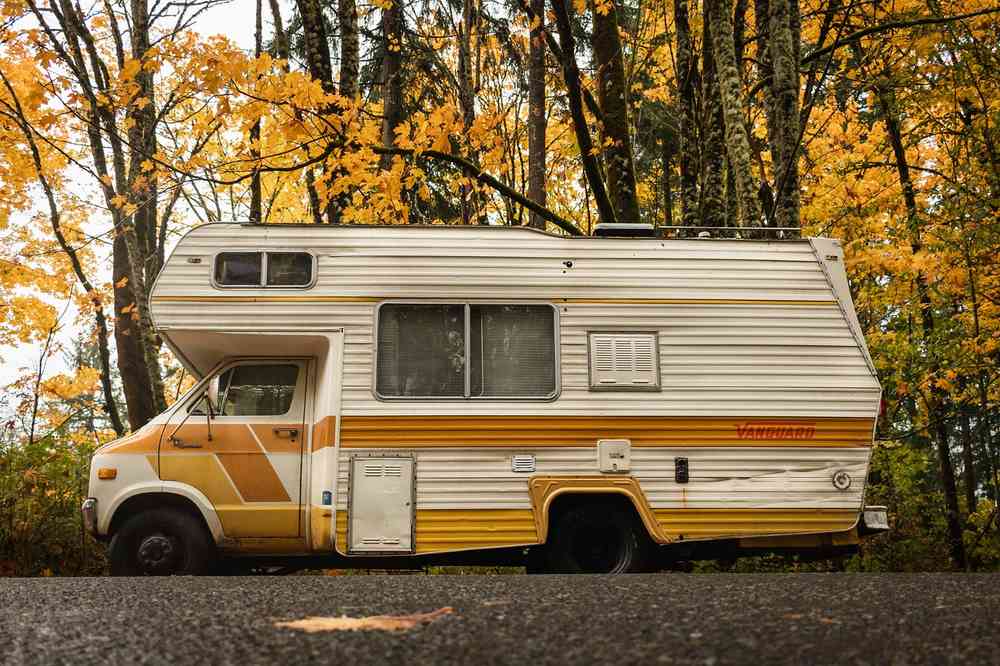 Camion‑moteur vintage garé sur route au milieu d'arbres aux feuilles jaunes