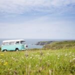 Camping-car blanc garé dans prairie fleurie face à la mer et falaises côtières