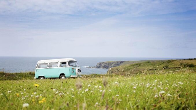 Camping-car blanc garé dans prairie fleurie face à la mer et falaises côtières