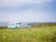 Camping-car blanc garé dans prairie fleurie face à la mer et falaises côtières